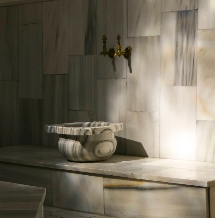 Veined marble kurna basin beneath traditional brass taps inside Ürgüp Hamam.